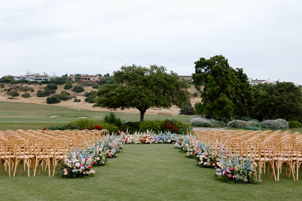 outdoor wedding ceremony area with chairs, floral arrangements, and a large oak tree at the Santaluz Club in San Diego