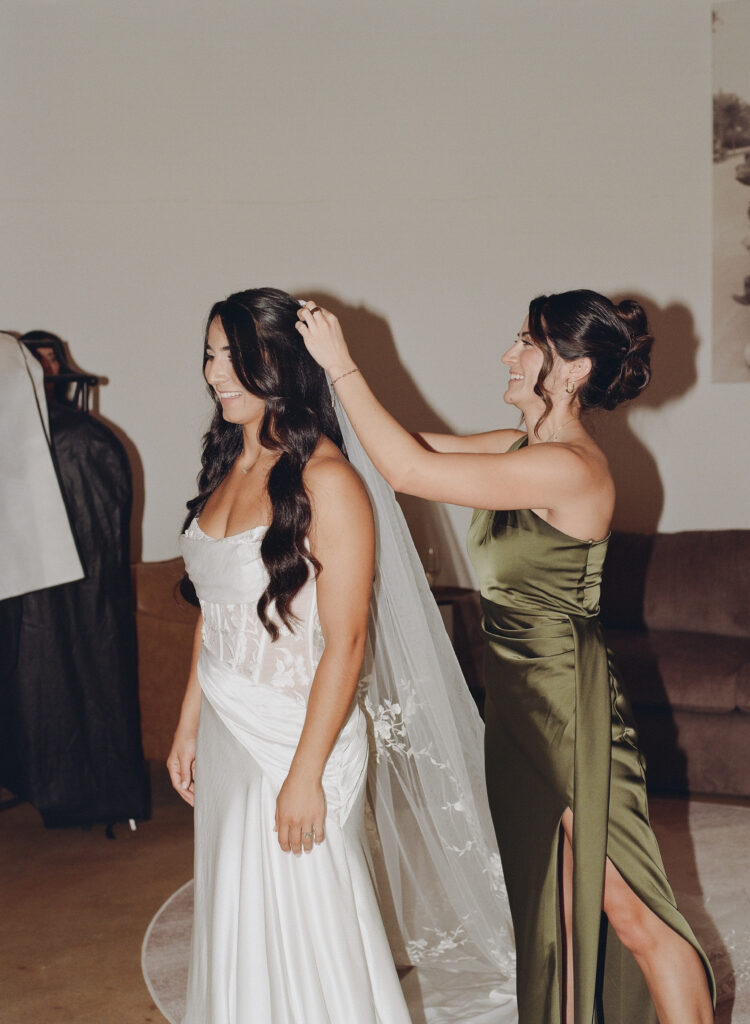 Bride having her veil adjusted by a bridesmaid while getting ready

