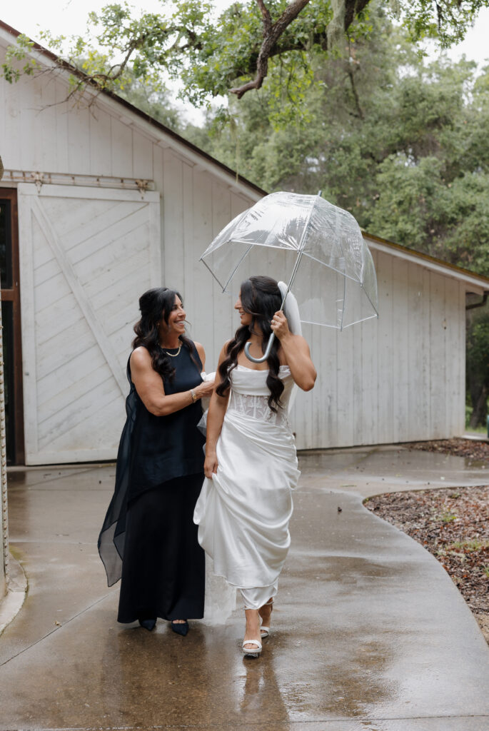Bride walking with a family member under a clear umbrella outside the Halter Ranch barn