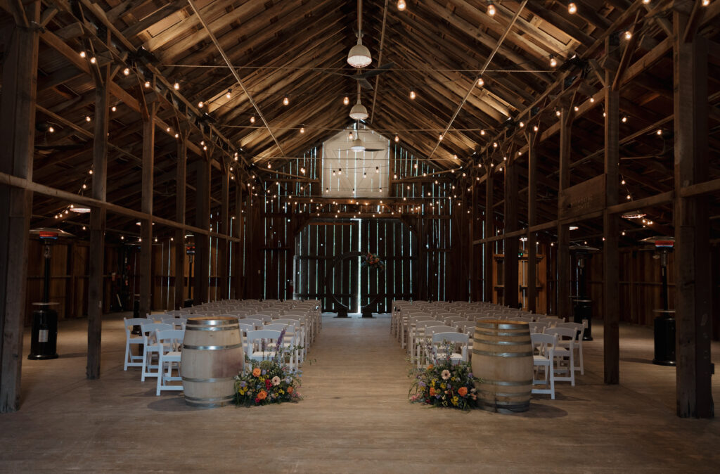 Wedding ceremony setup inside the Halter Ranch barn with white chairs, wine barrels, flowers, and string lights