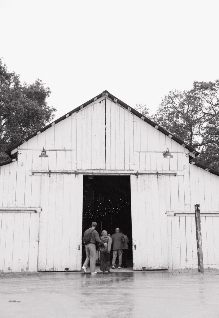 Guests walking into the white barn for a rainy wedding ceremony at Halter Ranch