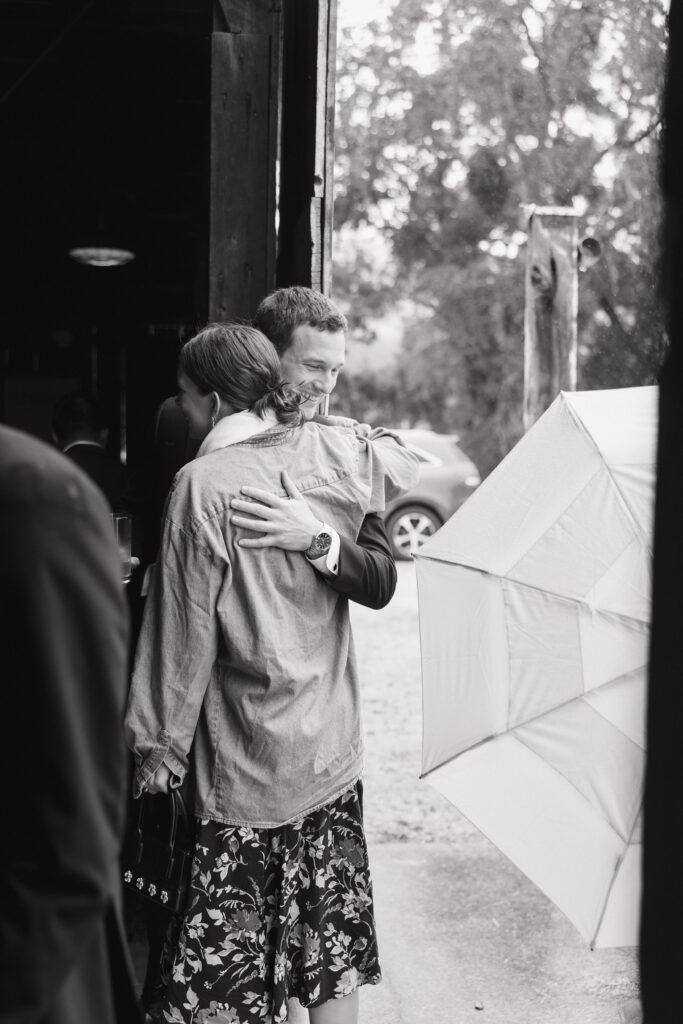Wedding guest embracing the groom outside the barn during a rainy Halter Ranch wedding day