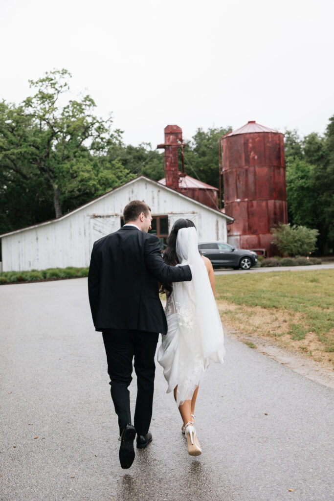 Bride and groom walking together toward the Halter Ranch barn in the rain