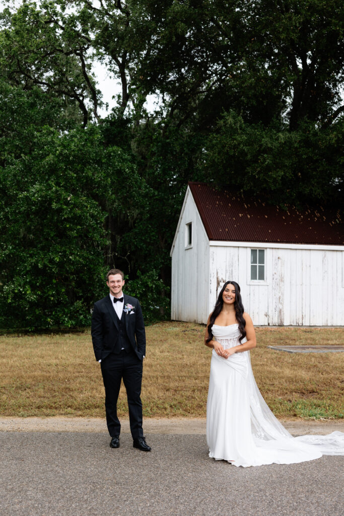 Bride and groom standing separately in front of a white barn at Halter Ranch