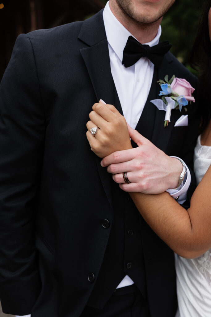Close-up of the bride’s hand resting on the groom’s tuxedo jacket and wedding boutonniere