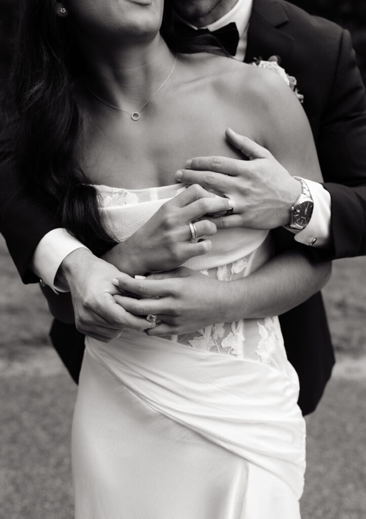 Black-and-white close-up of the newlyweds embracing and showing their wedding rings