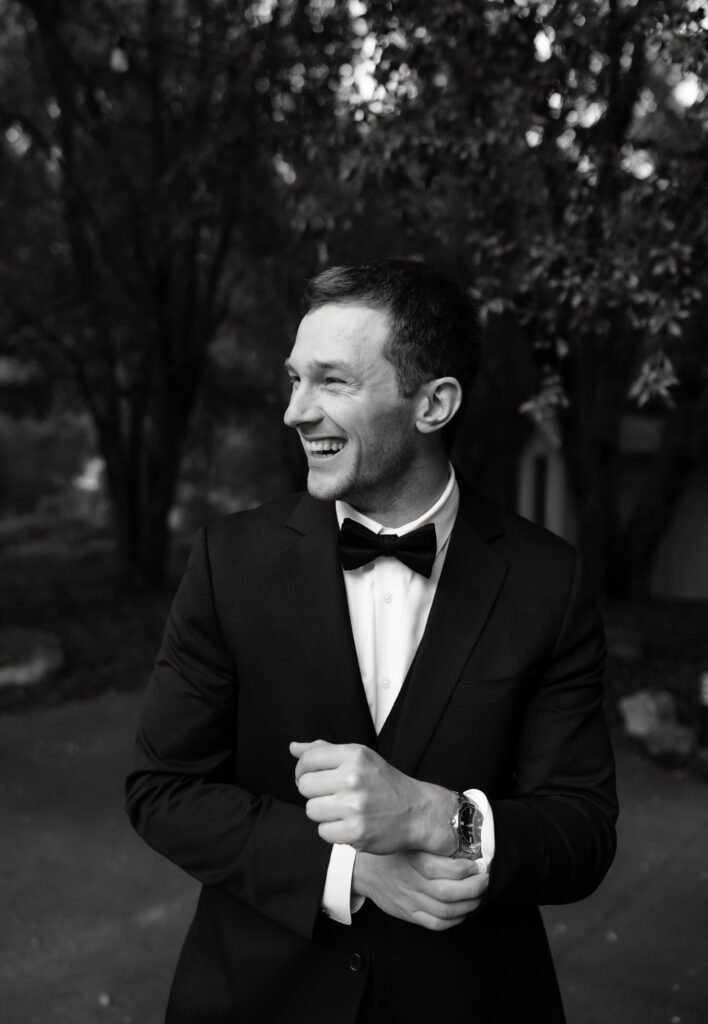 Black-and-white portrait of the groom adjusting his tuxedo cuff before the wedding ceremony