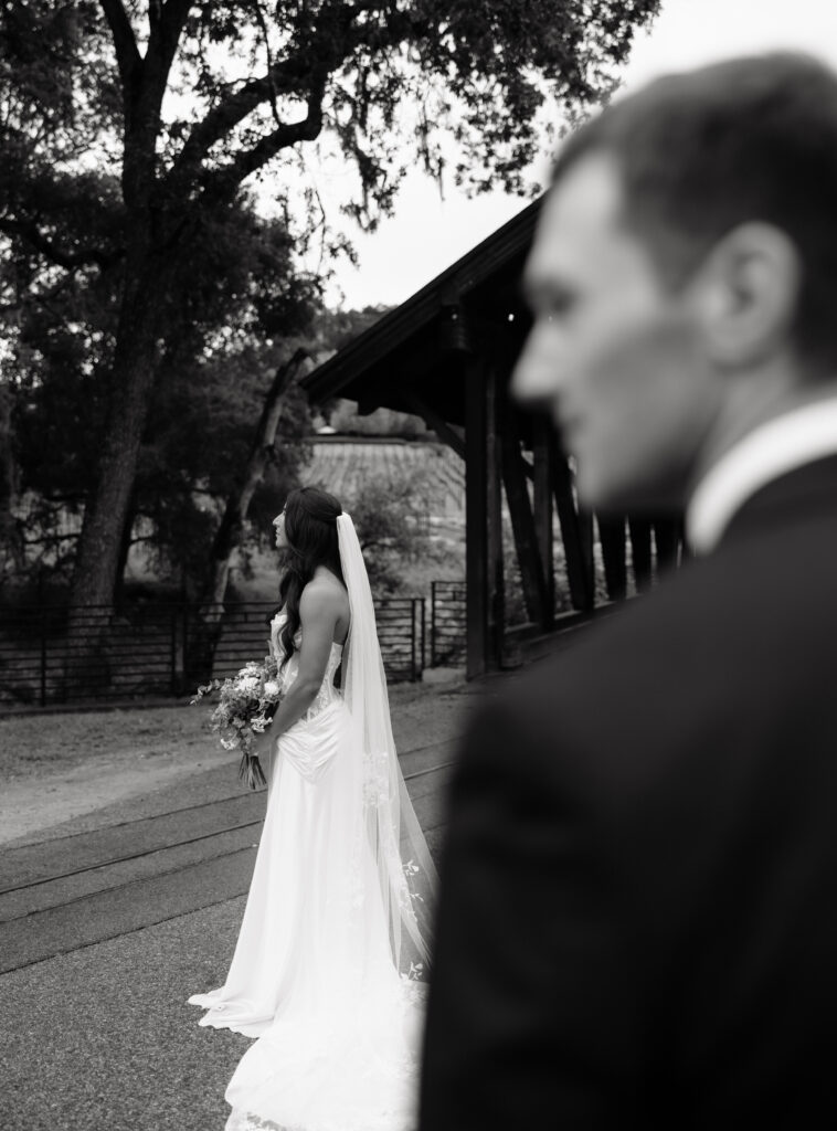 Black-and-white portrait of the bride standing with her bouquet near the covered bridge