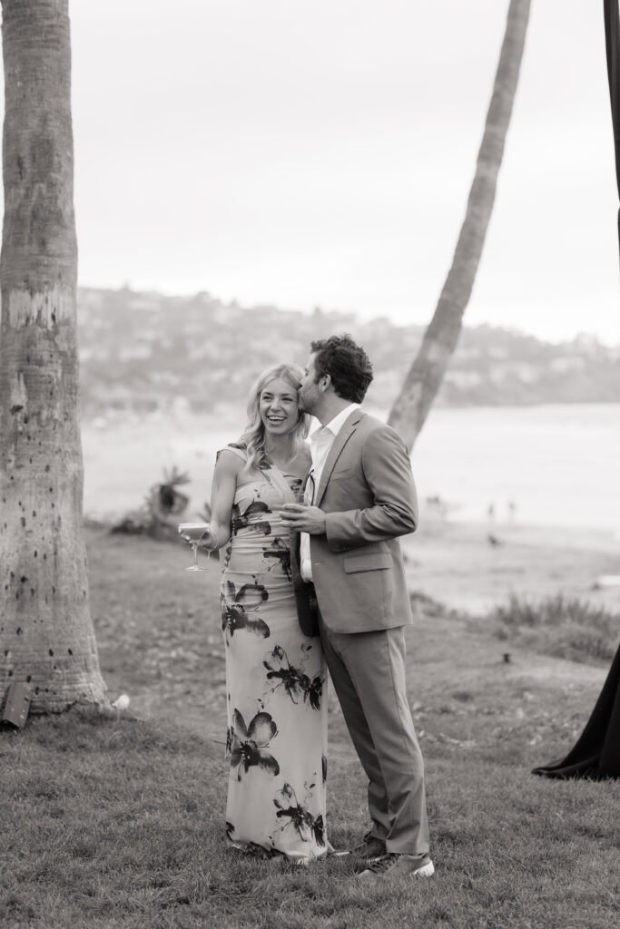 Wedding guest in a floral dress enjoying a cocktail with the Pacific Ocean behind her