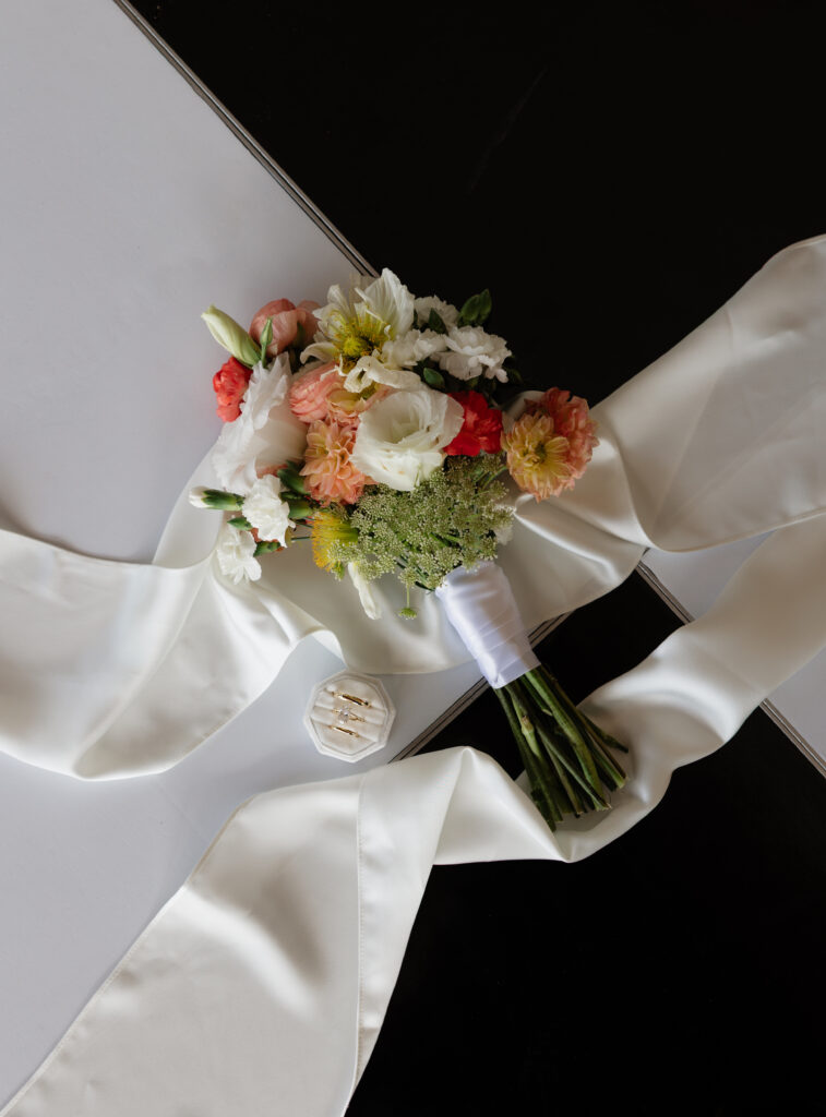 Bride and groom’s colorful wedding bouquet and rings styled with silk ribbon