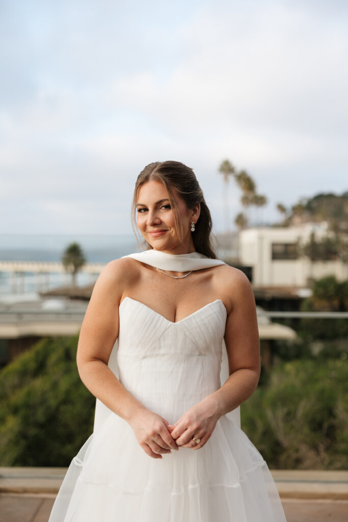 Bride smiling in her wedding dress with the La Jolla coastline behind her