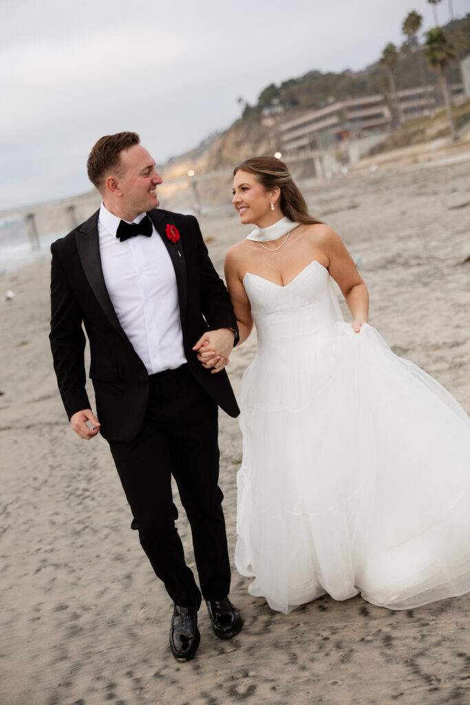 Bride and groom walking hand in hand along the La Jolla beach with the Pacific Ocean behind them